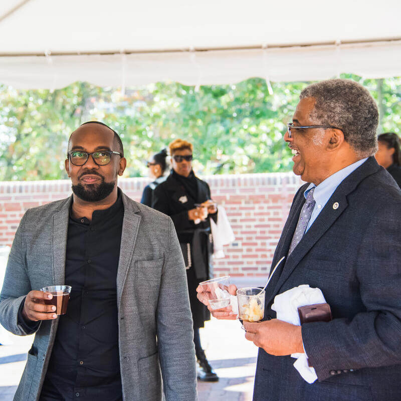 Howard staff smiling and eating while at an event outside near the Wayne A. I. Frederick Undergraduate Library