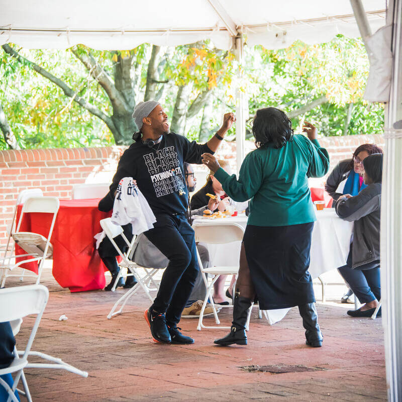 Howard staff smiling and dancing at a university celebration on a sunny day outside.